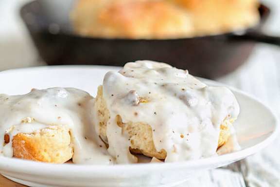 Two biscuits covered in white gravy on a white plate.