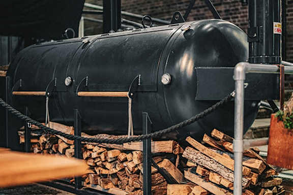 A large black smokestack is surrounded by logs and ropes.
