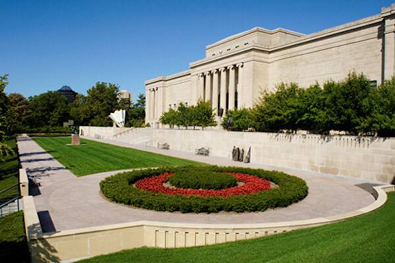 A large building with a long white wall and a circular flower bed in front of it.