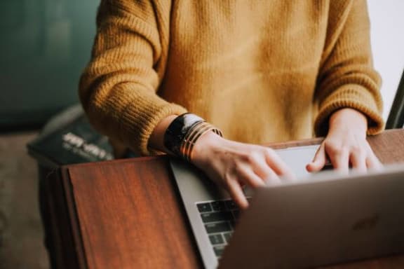a person in an orange sweater typing on a laptop
