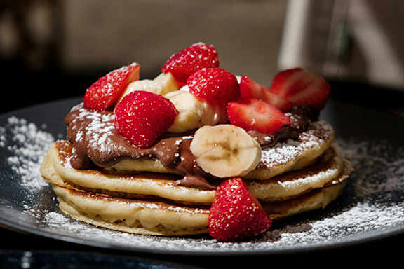 A stack of pancakes topped with strawberries, banana slices, and chocolate sauce.