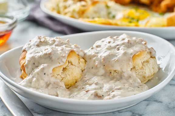Two biscuits covered in gravy are on a white plate.
