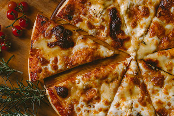 A pizza with cheese and tomatoes is cut into slices and served on a wooden board.