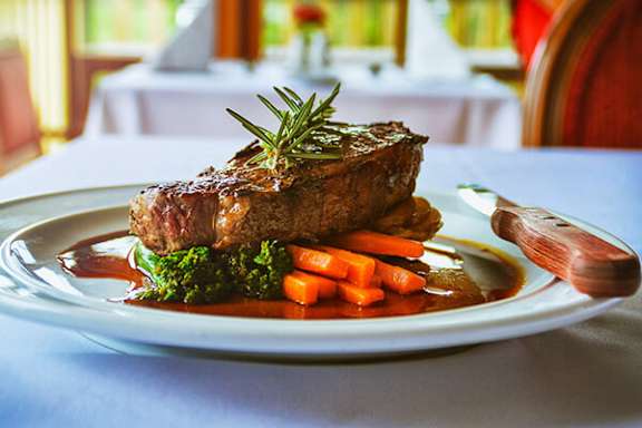 A steak with a sprig of rosemary on top is served on a white plate with carrots and broccoli.