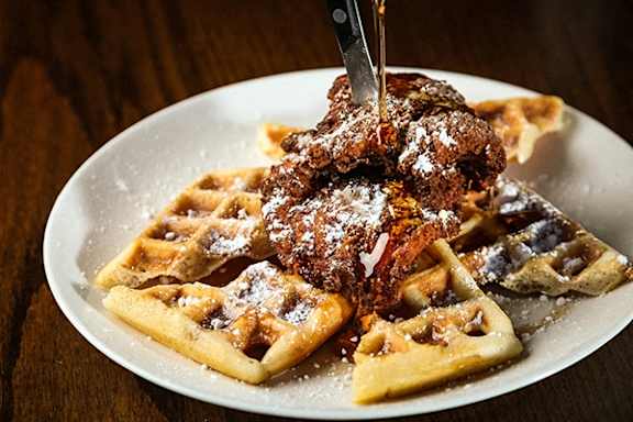 a plate of chicken and waffles with syrup and a knife