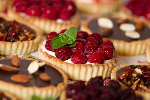 A close up of several tart desserts with berries and nuts.