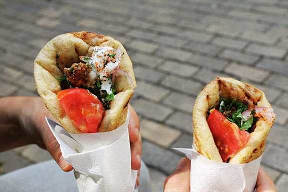 Two hands holding pita sandwiches with tomato and cheese.