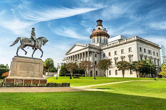 A statue of a man on a horse stands in front of a large white building with a dome.
