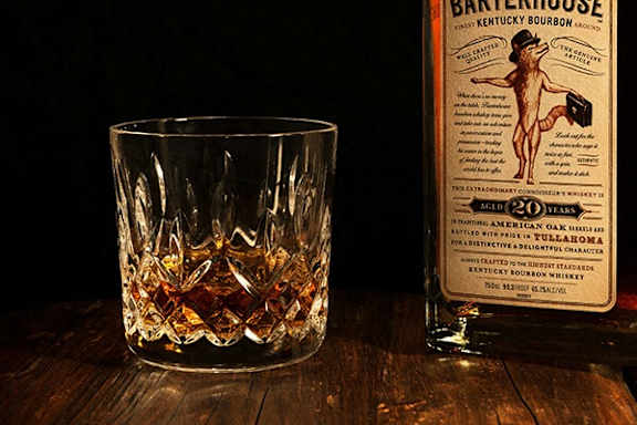 A glass of whiskey is next to a bottle of Bartlett House Kentucky Bourbon Whiskey.