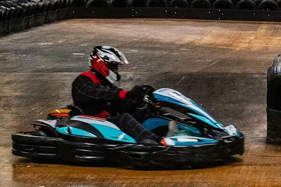 A person in a go-kart race is wearing a helmet and a red and black outfit.