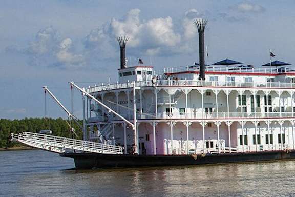 A large white riverboat with multiple decks is docked on the water.