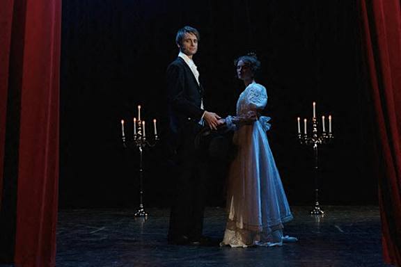 A man and a woman are standing on a stage, holding hands.
