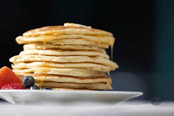 A stack of pancakes with syrup and berries on a white plate.