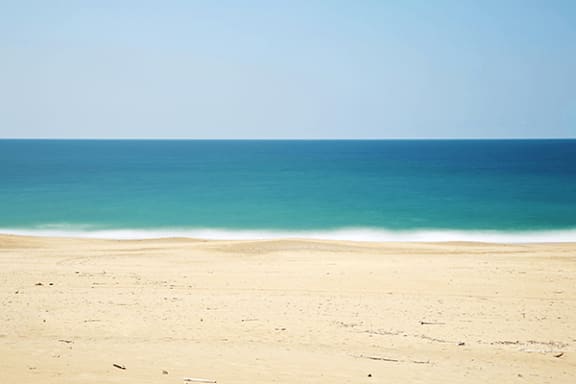 A sandy beach with a clear blue sky and calm sea.