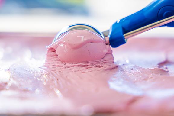 A blue spatula is spreading pink icing on a surface.