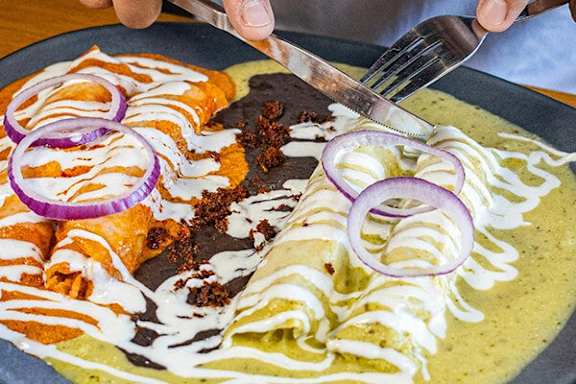 A plate of enchiladas topped with red onion slices and a creamy sauce.