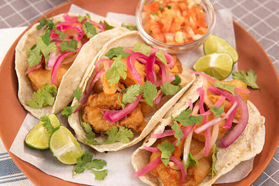 Three tacos with red onions and cilantro on a plate.