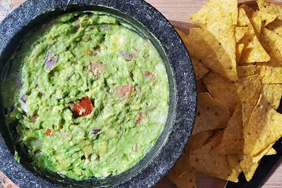 A bowl of guacamole with tortilla chips on the side.