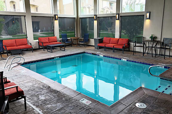 A large indoor swimming pool with a red couch and chairs around it.