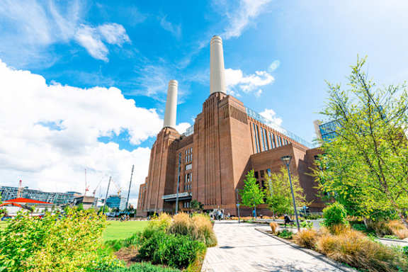 A large, modern building with two tall chimneys is surrounded by greenery.