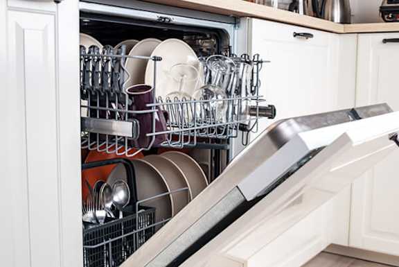 A dishwasher full of dishes is open and in front of a white cabinet.