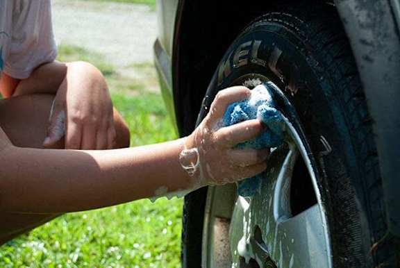 A person washing a car tire with a sponge.