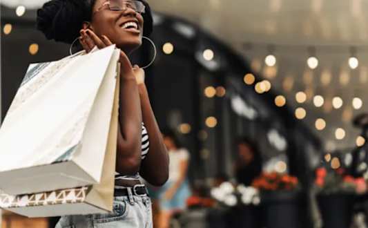 A woman with a shopping bag is standing in a brightly lit area.