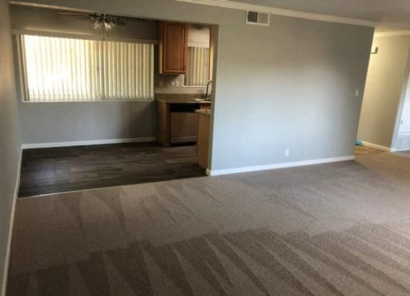 A room with a carpeted floor and a kitchenette in the corner.