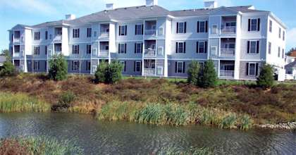 A large white building with a grey roof is situated next to a body of water.