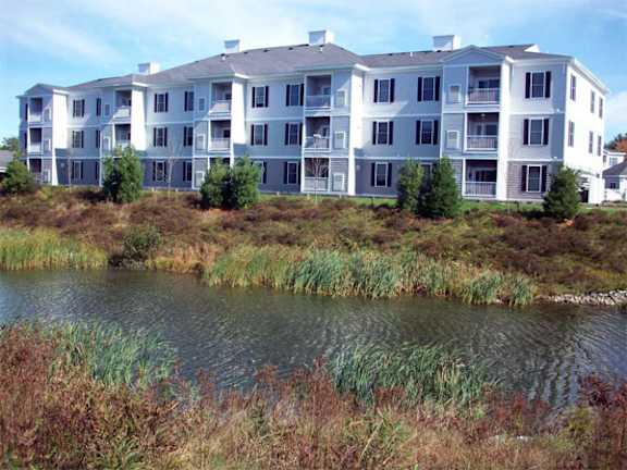 A large white building with a grey roof is situated next to a body of water.