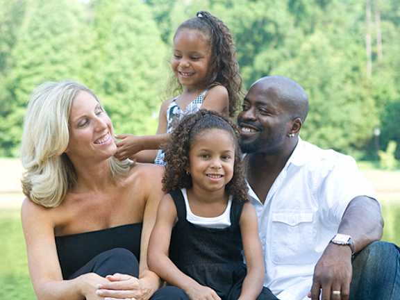 A family of four are sitting on a grassy area.
