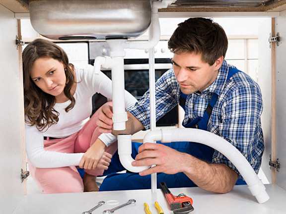 A man and a woman are fixing a sink.