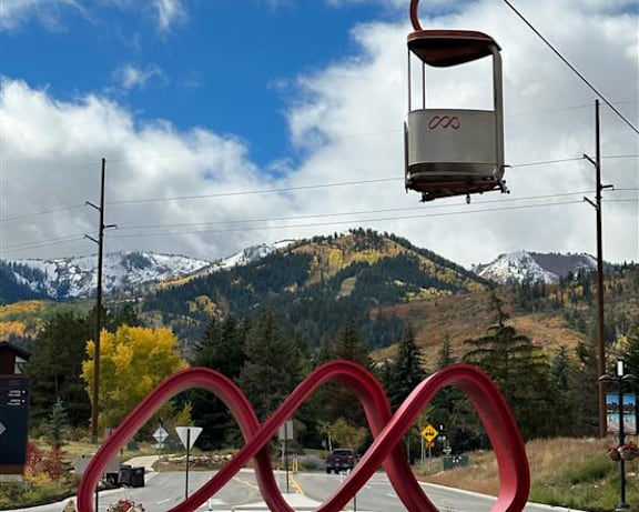 A cable car is suspended above a road with a large red infinity sign in the foreground.