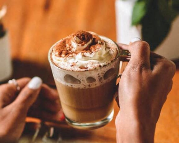 a person holding a cup of coffee with whipped cream