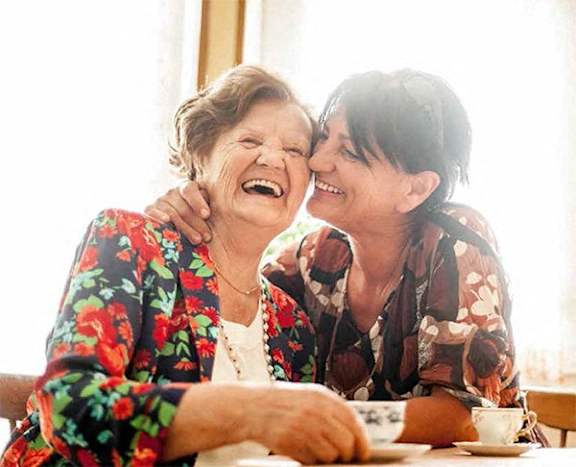 two elderly women laughing at a table with a cup of coffee