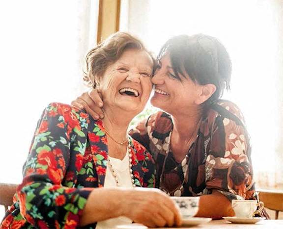 two elderly women laughing at a table with a cup of coffee