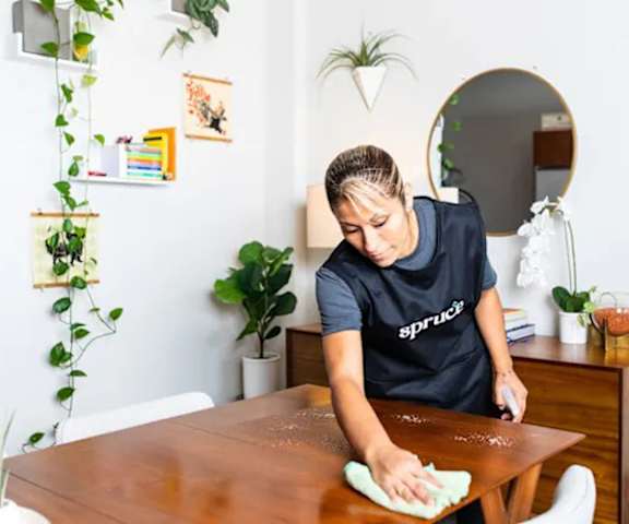 A woman in a black shirt is cleaning a wooden table with a green cloth.