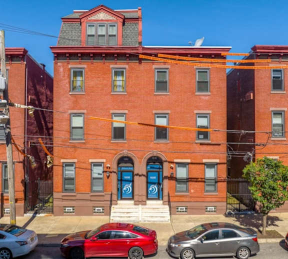A red car is parked in front of a brick building with a blue door.