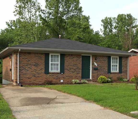 A house with a brick facade and a white door is surrounded by green bushes.