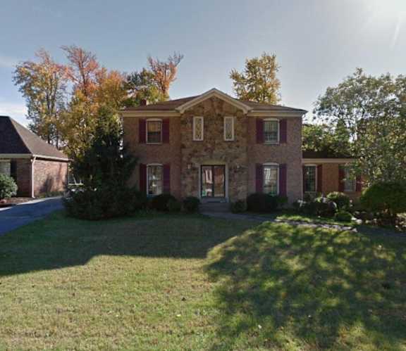 A large house with a red brick exterior and a large lawn in front.