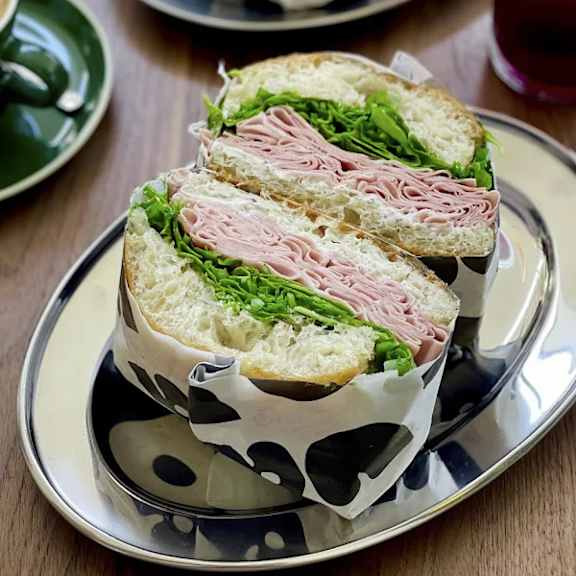 A sandwich with ham and lettuce is wrapped in a black and white patterned paper.