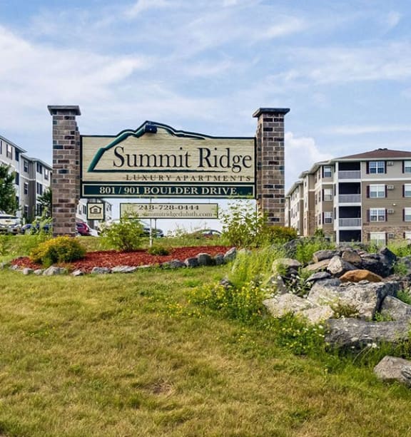 a sign for summit apartments in front of grass and rocks