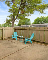 a patio with two blue chairs and a table in front of a fence