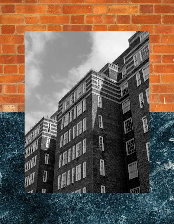 A black and white photo of a tall building is framed by a brick wall.