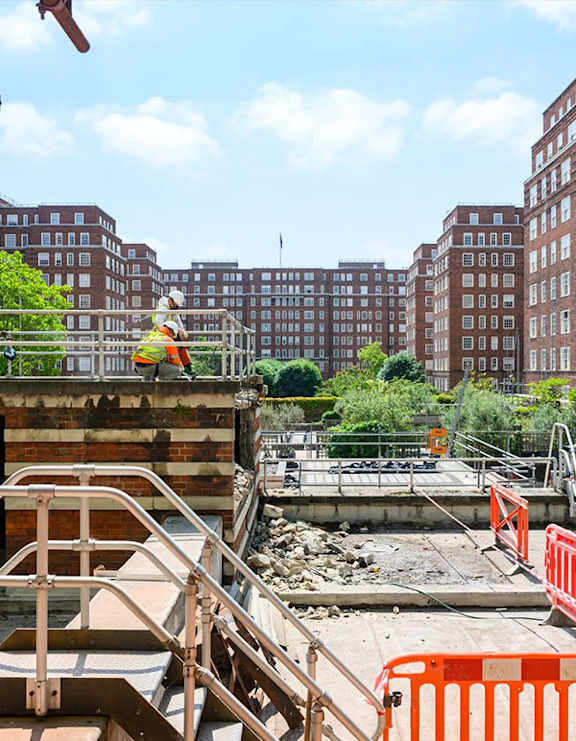 A construction worker is on a building site with a red and white striped barrier in the foreground.