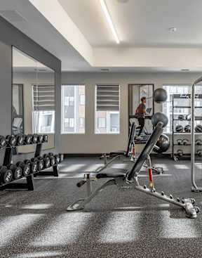 A gym with a variety of equipment including weights and cardio machines.at Vibe Apartments at Arbour Lake, Calgary Alberta