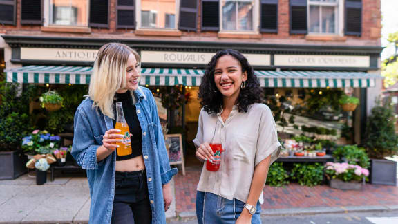 two women walking down the street holding drinks