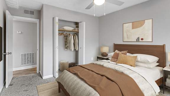 A bedroom with a large bed and a closet with clothes hanging.