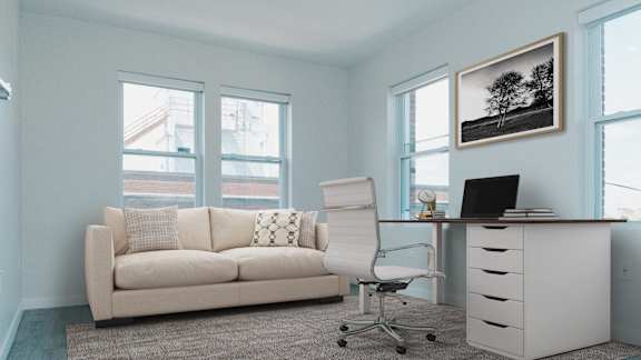 A white couch with pillows sits in a room with a desk and chair.