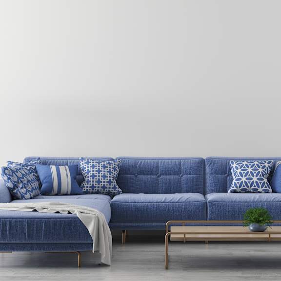A blue sofa with pillows and a blanket is in the foreground with a lamp and a plant in the background.